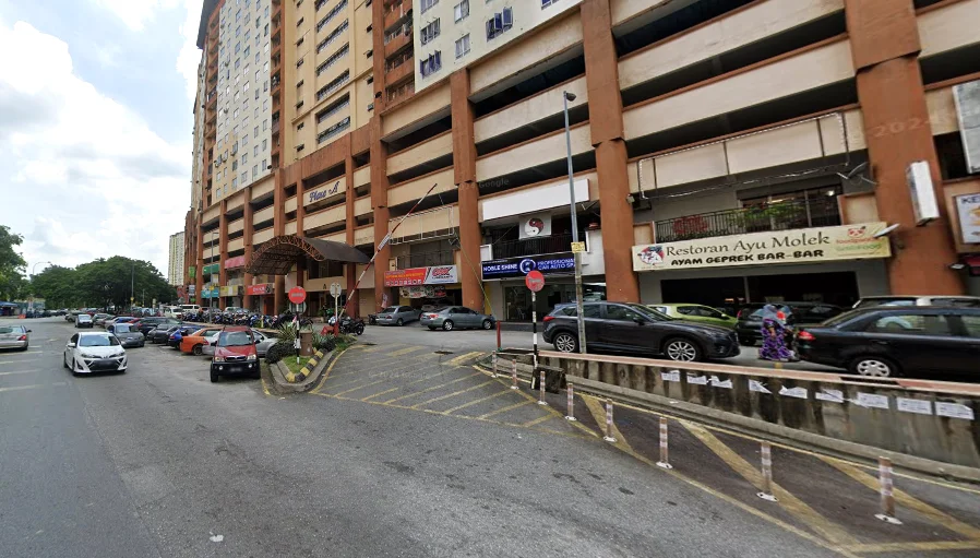 Exterior type: mid-rise condominium; features: multi-storey car park, ground-level retail shops, covered entrance with awning, signage for restaurants and shops, parking lot with marked spaces, surrounding greenery, urban street view, pedestrian walkway; style: modern.